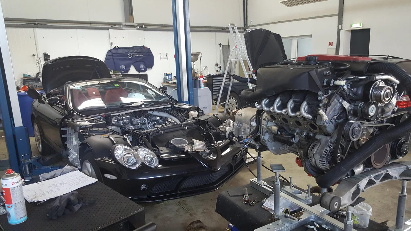 Fahrzeug mit geöffneter Motorhaube neben ausgebautem Motor in der Werkstatt